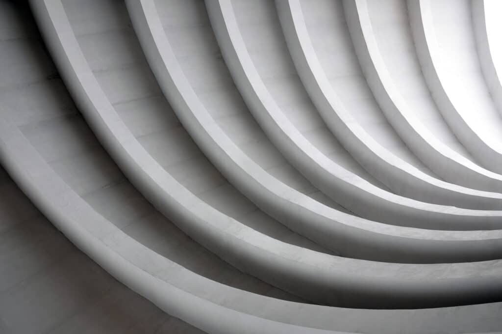 Architectural background. Modern white concrete arched composition of city bridge in perspective. Semicircular shapes. The light in the end.